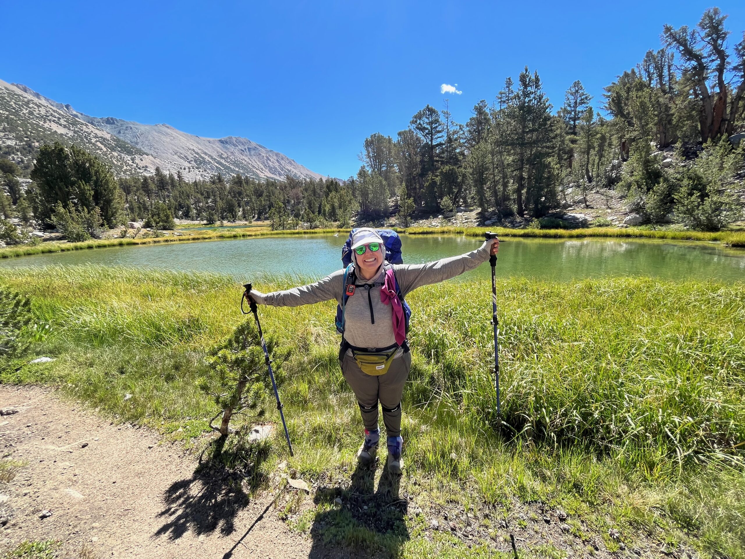 Katie in hiking gear infront of pond and mountains.